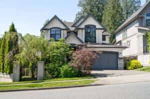 Front view of a modern two-story house with twin peaked roofs, dark trim, and a two-car garage, gated yard, and Kingston Street sign nearby.